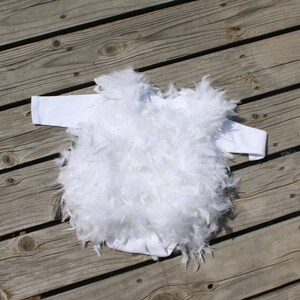 May include: White baby onesie with a fluffy white feather trim. The onesie is made of soft, comfortable fabric and is perfect for a special occasion.