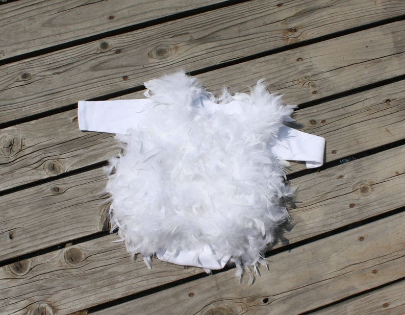 May include: White baby onesie with a fluffy white feather trim. The onesie is made of soft, comfortable fabric and is perfect for a special occasion.