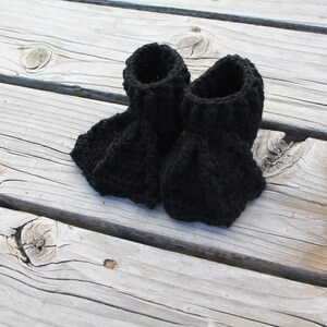 May include: A pair of black crocheted booties. The booties are made with a chunky yarn and have a simple, classic design.