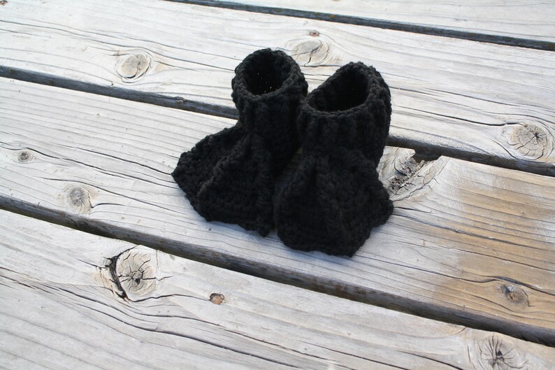 May include: A pair of black crocheted booties. The booties are made with a chunky yarn and have a simple, classic design.