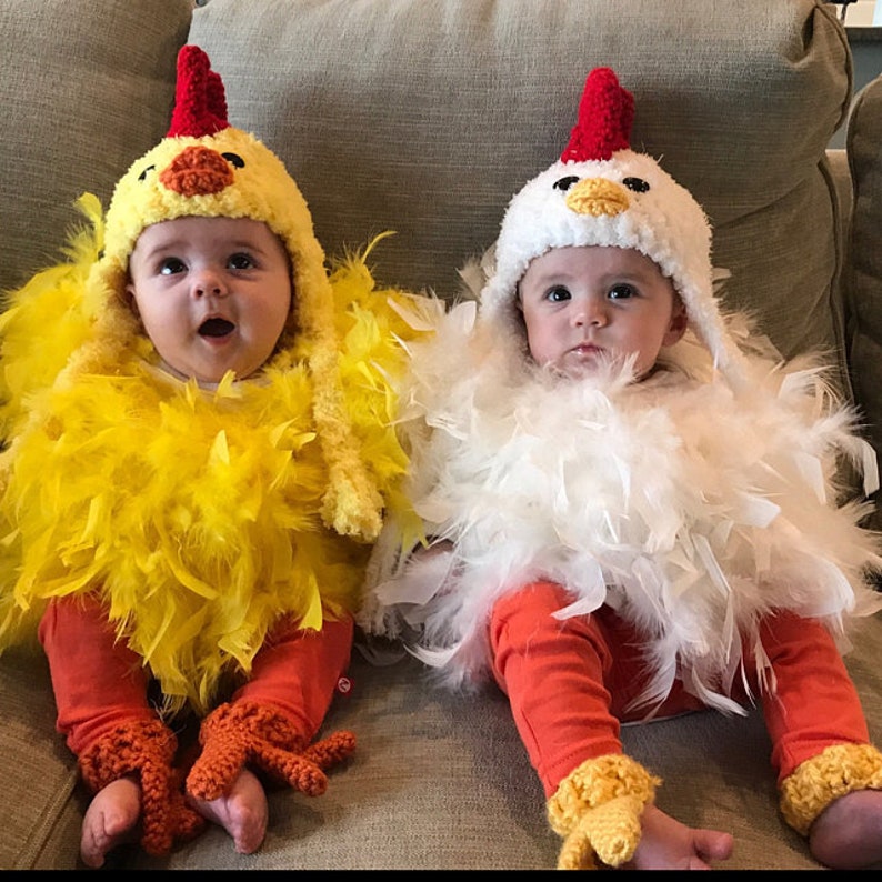 May include: Two babies dressed in chicken costumes. One baby is wearing a yellow chicken costume with yellow feathers and orange feet. The other baby is wearing a white chicken costume with white feathers and orange feet.