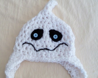 Puede incluir: Un gorro de ganchillo blanco con forma de fantasma, con la parte superior puntiaguda y dos orejeras. El gorro presenta dos parches oculares negros de ganchillo con botones azul claro cosidos en el centro y una boca negra bordada.