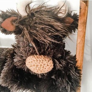 May include: A brown and black plush toy in the shape of a Highland cow with a crocheted nose and white horns.