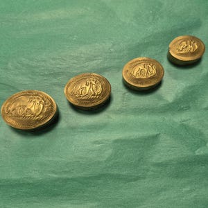 May include: Four antique brass oval boxes with detailed relief designs. Each box features a different scene, possibly depicting classical figures or animals. The boxes are arranged diagonally on a green surface, showcasing their intricate craftsmanship.