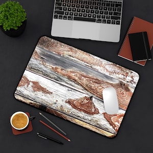 Op de afbeelding: Een rechthoekige muismat met een design van verweerde houtnerf in bruin, wit en grijs. Een witte computermuis ligt op de mat. Kantoorbenodigdheden omringen de mat.