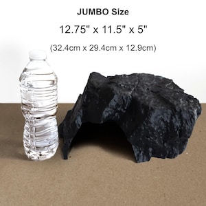 以下が含まれることがあります： 黒い岩のような装飾的な水槽の隠れ家で、サイズは32.4cm x 29.4cm x 12.9cmです。サイズの比較のために、透明な水筒が隠れ家の隣にあります。「JUMBO Size」の文字が上部にあります。