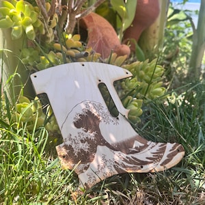 May include: A wooden guitar pickguard featuring a detailed wood-burned image of Hokusai's "The Great Wave off Kanagawa." The pickguard is light-colored with a natural wood grain and has several pre-drilled holes for mounting.