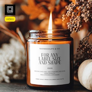 May include: A lit candle in a glass jar with a white label that reads "FOR ANY LABEL SIZE AND SHAPE". The candle is 250g and made with natural essential oils and coffee grounds. The background is blurred with fall foliage.