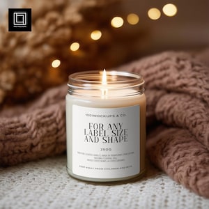 Peut inclure: Une bougie allumée dans un pot en verre transparent avec une étiquette blanche. L'étiquette indique "FOR ANY LABEL SIZE AND SHAPE" et "250g". La bougie est entourée d'un tissu marron doux et texturé. L'arrière-plan présente des lumières floues.