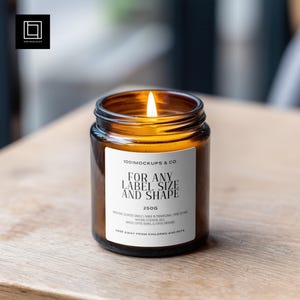 Op de afbeelding: Een brandende, amberkleurige kaars in een glazen pot met een wit etiket. Op het etiket staat "FOR ANY LABEL SIZE AND SHAPE" en "250G". De kaars staat op een houten oppervlak. De kaars is een niet-giftige geurkaars.