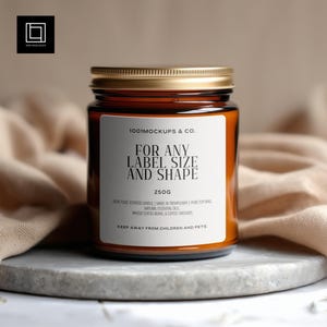 Peut inclure: Un bougeoir en verre marron avec un couvercle doré et une étiquette blanche. L'étiquette indique "FOR ANY LABEL SIZE AND SHAPE" et "250g". La bougie est sur une surface en pierre grise. Le texte "1001 MOCKUPS & CO." est également visible.