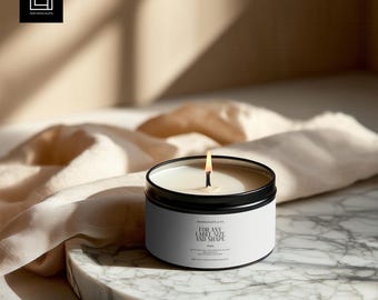 May include: A lit, round candle in a black metal container with a white label. The label reads "FOR ANY LABEL SIZE AND SHAPE". The candle sits on a marble tray with a beige cloth in the background. The flame is lit and casting a warm glow.
