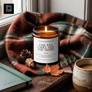 May include: A lit amber glass candle with a white label reading 1001MOCKUPS & CO. FOR ANY LABEL SIZE AND SHAPE 250G. The candle features a visible flame and is surrounded by pinecones, a dried leaf, and a plaid fabric.
