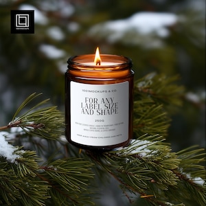 May include: A burning candle in a brown glass jar with a white label. The label says "FOR ANY LABEL SIZE AND SHAPE" and "250G". The candle sits on a pine branch. The background is a blurred view of a snowy forest.
