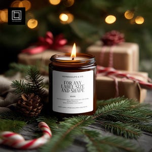 Op de afbeelding: Een brandende bruine glazen kaarsenpot met een wit etiket met de tekst "FOR ANY LABEL SIZE AND SHAPE". De kaars staat op een bedje van dennennaalden, met een dennenappel en ingepakte cadeaus op de achtergrond. De kaars is 250g.
