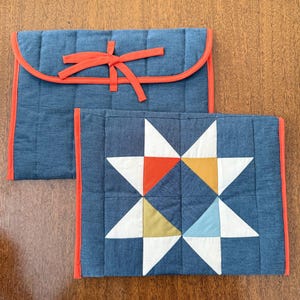 May include: Two denim-colored quilted fabric cases with orange trim. One case has a curved flap with an orange bow closure. The other case features a star pattern with white, orange, yellow, and blue triangles.