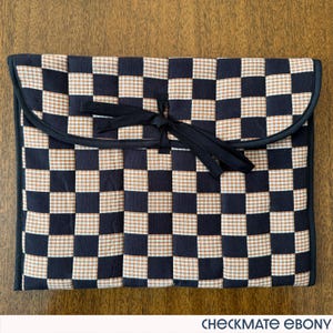 May include: A black, tan, and white checkered fabric case with a black trim and a black tie closure. The case is rectangular with rounded corners and the text "CHECKMATE EBONY" is at the bottom.