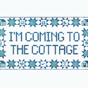 Puede incluir: Un edredón blanco con detalles azules y el texto "I'M COMING TO THE COTTAGE." El edredón presenta un borde de patrones de estrellas azules y pequeños diseños de casas e iconos. El diseño tiene un tema acogedor de cabaña.