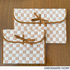 May include: Two ivory and brown checkered fabric pouches with rounded edges and brown ribbon ties. The pouches are different sizes and are made of a quilted material. The text "CHECKMATE IVORY" is at the bottom.