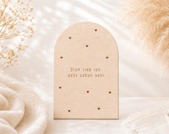 Könnte beinhalten: Eine bogenförmige Holztafel in heller Farbe mit der eingravierten deutschen Aufschrift "Dich lieb ich echt schon sehr." und kleinen herzförmigen Ausschnitten, die über die Oberfläche verteilt sind. Die Tafel hat eine glatte Oberfläche.