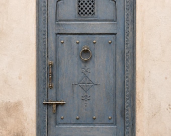 Puerta marroquí azul lavada, entrada de riad tallada a mano, aldaba de latón, ventana enrejada.