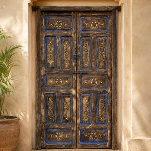 Può includere: Una doppia porta in legno invecchiato con intagli intricati e finitura blu e oro. La porta presenta disegni geometrici e floreali ornati, su una parete dai toni caldi e neutri. La porta è incorniciata da un arco decorativo.