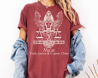 May include: A maroon t-shirt featuring a white graphic of a winged figure with scales and the text "Ma'at Truth, Justice & Cosmic Order." The shirt has rolled-up sleeves and a relaxed fit.