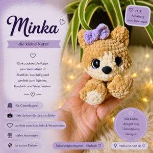 Puede incluir: Un pequeño juguete de peluche de gato tejido a ganchillo en color beige y crema con un lazo morado en la cabeza, ojos grandes y oscuros y una nariz negra. La imagen incluye texto en alemán, como 'Minka', 'die kleine Katze' y 'PDF Anleitung zum Download'.