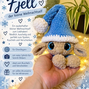 Könnte beinhalten: Ein gehäkeltes Plüschtier mit beigem Körper, großen blauen Augen und einer blauen Zipfelmütze mit weißem Bommel und Rand. Das Bild enthält den Text Fjell der kleine Weihnachtself sowie Schneeflockengrafiken und verschiedene Symbole.