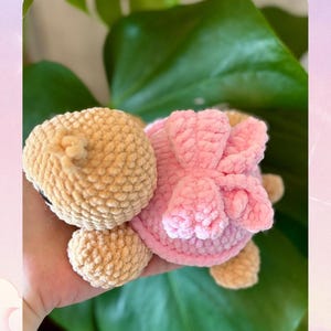 Könnte beinhalten: Ein gehäkeltes Plüschtier in Form eines Bären mit einer rosa Schleife. Der Bär ist beige und die Schleife ist rosa. Das Bild enthält auch den Text "MINI LUMY" und deutschen Text über digitale Häkelanleitungen.