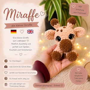 Könnte beinhalten: Ein kleines, gehäkeltes Giraffen-Kuscheltier aus hellbraunem und dunkelbraunem Chenillegarn. Die Giraffe hat große, dunkle, glänzende Augen mit langen Wimpern, zwei kleine Hörner und abgerundete Ohren. Der Text Miraffe die kleine Giraffe ist zu sehen.