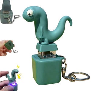 May include: A teal-colored dinosaur-shaped keychain with a large eye and a curved tail. The dinosaur sits atop a square base with a clear, rectangular light. A silver keyring and clasp are attached to the base.