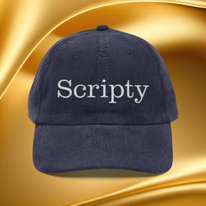 Op de afbeelding: Marineblauwe corduroy baseballpet met het woord "Scripty" in wit geborduurd. De pet heeft een gebogen klep en een ronde kroon. De achtergrond is goudkleurig.