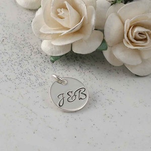 May include: A silver charm with the initials "J&B" engraved in a cursive font.