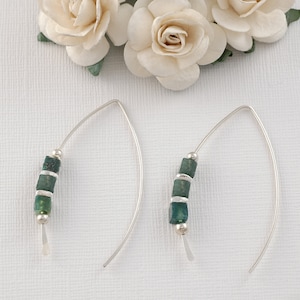 May include: A pair of silver earrings with a curved wire design. Each earring features a row of four green glass beads.
