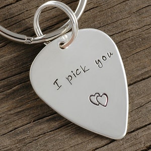 May include: Silver guitar pick keychain with the words "I pick you" and two hearts engraved on it.