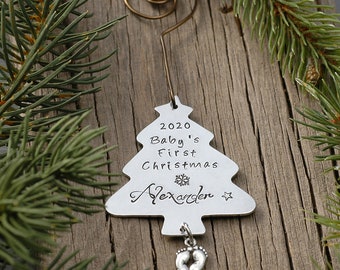 May include: Silver Christmas tree ornament with the text "2020 Baby's First Christmas Alexander" and a small silver charm of baby footprints hanging from the bottom.