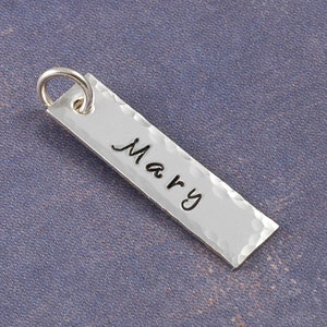 May include: Silver charm with a hammered finish and the name "Mary" engraved on it.