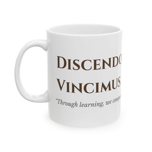 May include: White ceramic coffee mug with the words "DISCENDO VINCIMUS" in brown lettering. Below the text is the quote, "Through learning, we conquer."