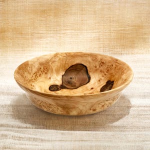 Puede incluir: Un cuenco redondo de madera de ra&iacute;z de color claro, con un acabado liso y pulido. El interior muestra patrones de nudos org&aacute;nicos oscuros y prominentes, junto con texturas de vetas arremolinadas que contrastan con la superficie clara.