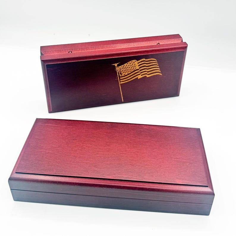 May include: Two wooden boxes with a rich, reddish-brown finish. One box is open, revealing a detailed engraving of an American flag. The other box is closed. The boxes are likely for storing keepsakes or small items.