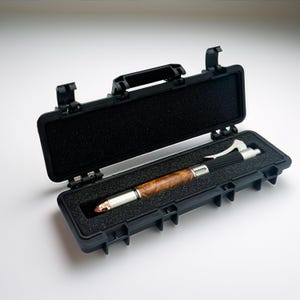 May include: A handcrafted pen with a wood grain barrel and silver accents rests in an open black case. The pen features a unique design with a textured grip and a decorative tip. The case is lined with black foam for protection.