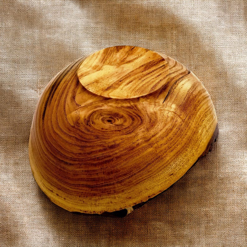 Op de afbeelding: Een ronde houten kom met een opvallend natuurlijk nerfpatroon in wervelende licht- en donkerbruine tinten. De kom heeft een glad, gepolijst oppervlak en een duidelijke ronde voet, die de organische textuur en de ringen van het hout laat zien.