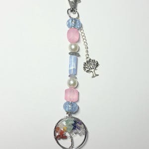 May include: A beaded keychain with a silver clasp and a tree of life charm. The keychain features a mix of pink, blue, and clear beads, along with a circular charm filled with colorful gemstones.