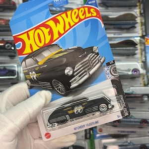 May include: A black '47 Chevy Fleetline Hot Wheels die-cast car in its original packaging. The car has yellow and black accents and the text "Goodyear" and "Rod Squad". The packaging is blue with the Hot Wheels logo.