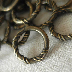 Pode incluir: Um close-up de uma pilha de anéis de salto de metal dourado antigo. Os anéis são torcidos e têm um design semelhante a uma corda.