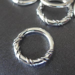 Pode incluir: Um close-up de um monte de argolas de salto prateadas com um design torcido. As argolas estão dispostas em um padrão aleatório sobre uma superfície cinza.