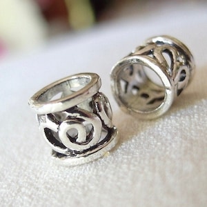 May include: Two silver metal bead spacers with an intricate design. The spacers are hollow and have a circular opening in the center.