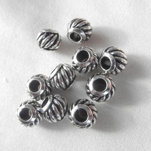 May include: A group of ten silver metal beads with a rope-like design. The beads have a hole in the center for stringing.