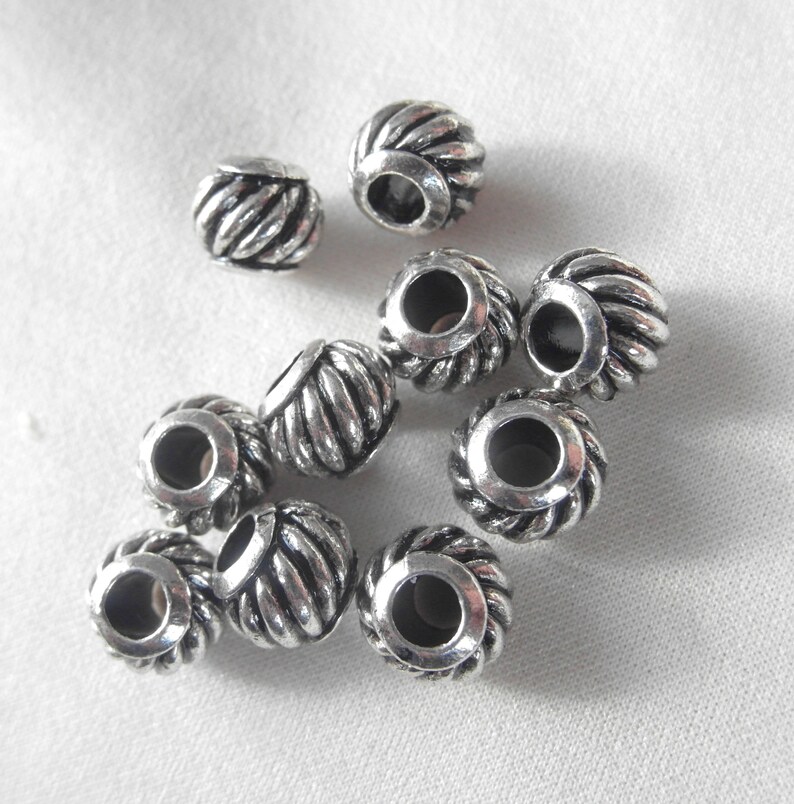 May include: A group of ten silver metal beads with a rope-like design. The beads have a hole in the center for stringing.